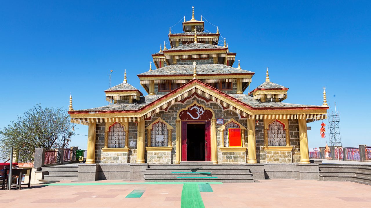 Surkanda Devi Temple with prayer flags and snow-capped mountains in the distance
